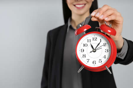 Businesswoman holding alarm clock on light gray background, closeup with space for text. Time managementの写真素材