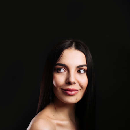 Portrait of happy young woman with beautiful black hair and charming smile on dark background, space...