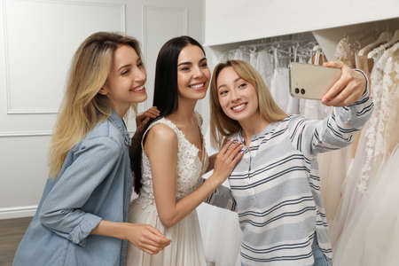 Friends taking selfie with bride wearing wedding dress in boutiqueの写真素材