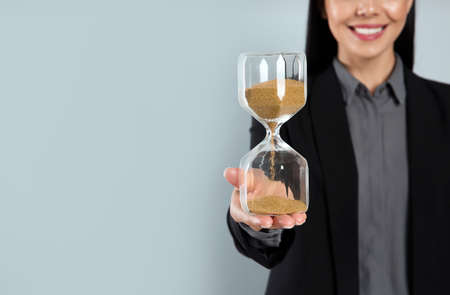 Businesswoman holding hourglass on light gray background, closeup with space for text. Time managementの写真素材