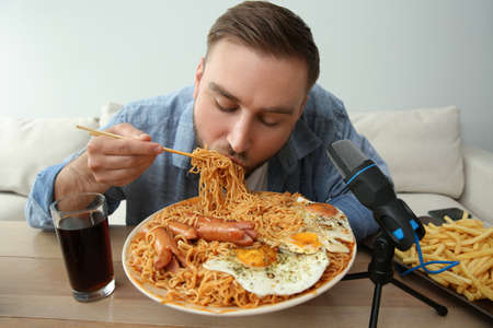 Food blogger eating in front of microphone at table against light background. Mukbang vlogの写真素材