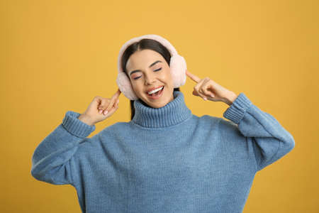 Beautiful young woman wearing earmuffs on yellow background