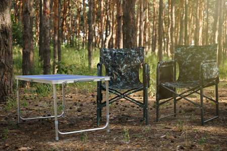 Camouflage chairs and table in forest on sunny day