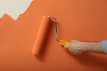 Man applying orange paint with roller brush on white wall, closeupの写真素材