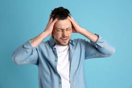 Man suffering from terrible migraine on light blue backgroundの写真素材