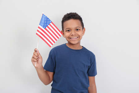 Happy African-American boy holding national flag on light background