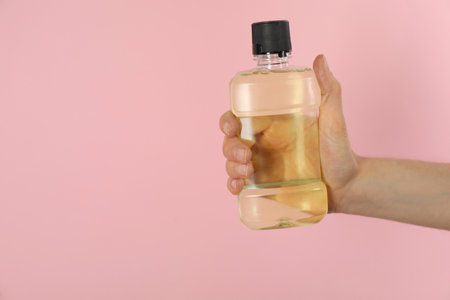 Woman holding bottle with mouthwash on pink background, closeup. Space for textの写真素材