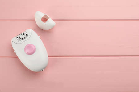 Modern epilator and cap on pink wooden table, flat lay. Space for textの写真素材