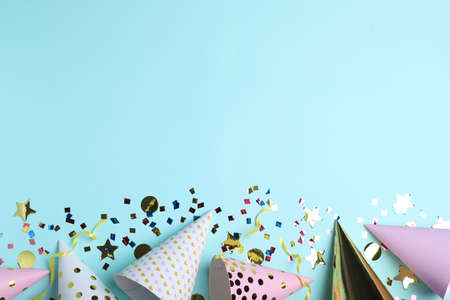 Flat lay composition with party hats and confetti on light blue background, space for text. Birthday...