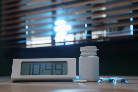 Digital alarm clock and pills on table indoors. Insomnia treatmentの写真素材
