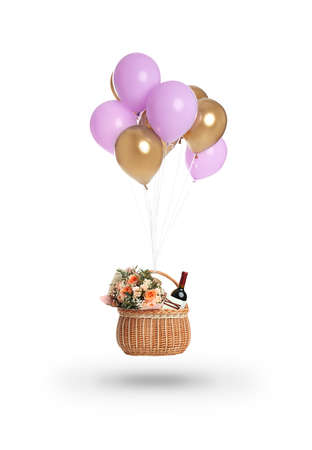 Bunch of color balloons and wicker basket with different gifts on white backgroundの写真素材