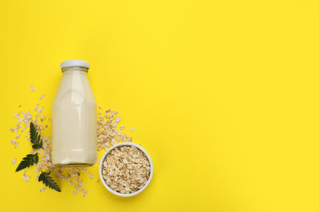 Vegan milk and oat flakes on yellow background, flat lay. Space for textの写真素材