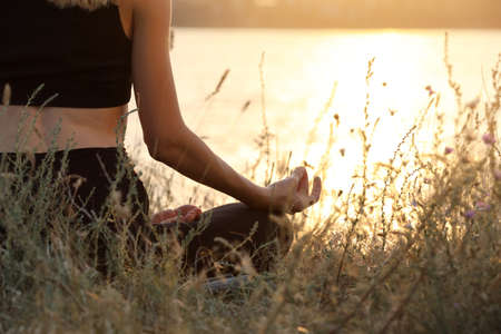 Young woman meditating near river at sunset, closeupの写真素材