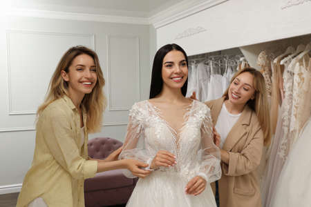 Bride with friends choosing wedding dress in boutique