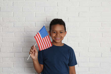 Happy African-American boy holding national flag near white brick wallの写真素材