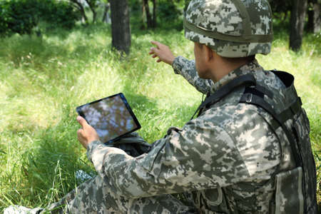 Soldier with backpack using tablet in forest