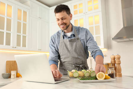 Man making dinner while watching online cooking course via laptop kitchenの写真素材