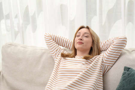 Beautiful young woman relaxing on sofa indoorsの写真素材