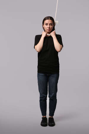 Depressed woman with rope noose on neck against light gray background