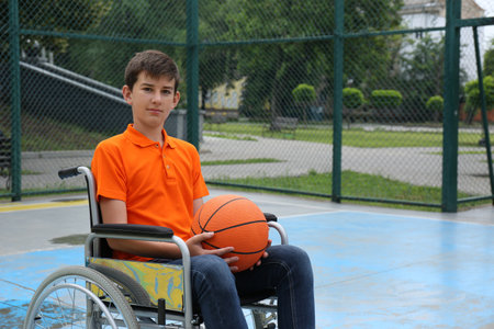 Disabled teenage boy in wheelchair with basketball ball at outdoor courtの写真素材