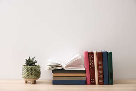 Collection of books and houseplant on wooden table near white wall. Space for textの写真素材