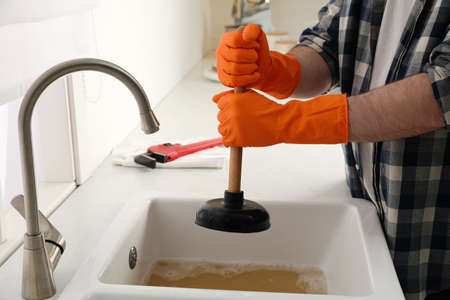 Man using plunger to unclog sink drain in kitchen, closeupの写真素材
