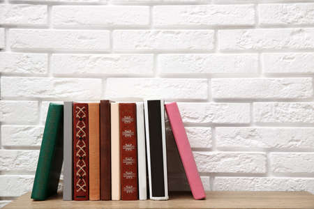 Collection of books on wooden table near white brick wall. Space for textの写真素材