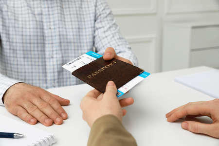 Manager giving passport and ticket to man at desk in travel agency office, closeupの写真素材