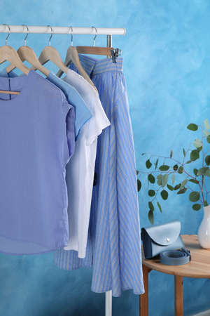 Rack with stylish clothes near light blue wall indoorsの写真素材