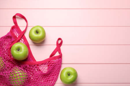 Net bag with fresh green apples on pink wooden table, flat lay. Space for textの写真素材