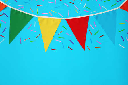 Bunting with colorful triangular flags and confetti on light blue background, flat lay. Space for textの写真素材