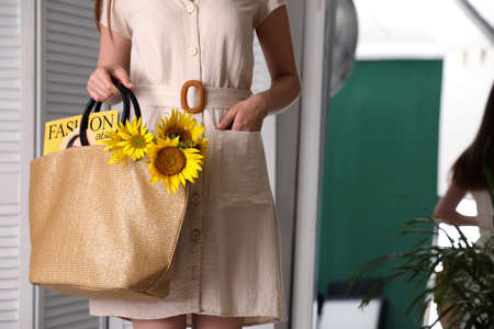 Woman holding beach bag with magazine and beautiful bouquet of sunflowers indoors, closeupの写真素材
