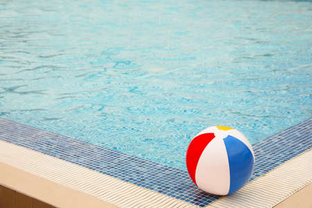 Inflatable colorful beach ball on edge of outdoor swimming pool, space for textの写真素材