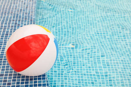 Inflatable colorful beach ball on edge of outdoor swimming pool, space for textの写真素材