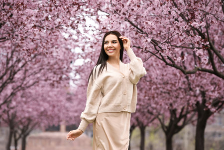 Pretty young woman in park with blooming trees. Spring lookの写真素材