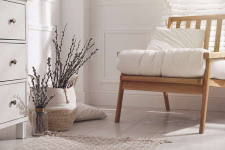 Pussy willow tree branches near chest of drawers and armchair in room
