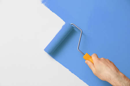 Man applying orange paint with roller brush on white wall, closeupの写真素材