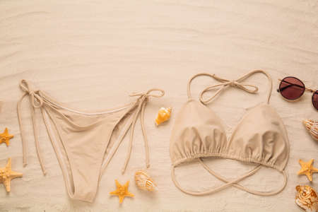 Stylish bikini, sunglasses, starfishes and shells on sand, flat lay. Space for text