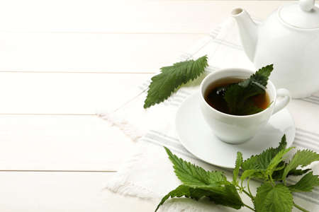 Aromatic nettle tea and green leaves on white wooden table, space for text