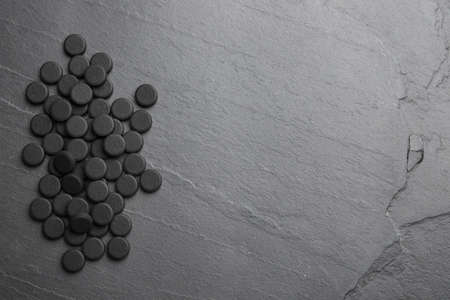 Pile of activated charcoal pills on black table, flat lay with space for text. Potent sorbentの写真素材