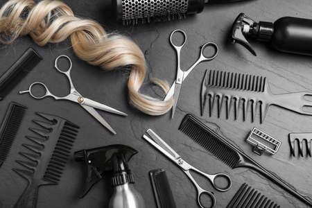Flat lay composition of professional scissors, hair strand and other hairdresser's equipment on black table. Haircut toolの写真素材