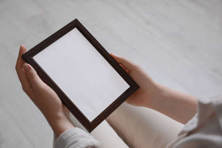 Woman holding empty photo frame indoors, closeup