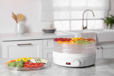 Cut fruits, vegetables and dehydrator machine on gray marble table in kitchen