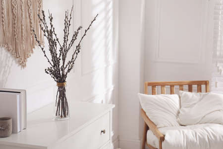 Glass vase with pussy willow tree branches on white chest of drawers in room, space for textの写真素材
