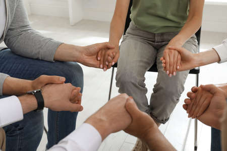 Psychotherapist and group of drug addicted people holding hands together at therapy session, closeupの写真素材