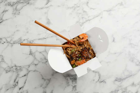 Box of wok noodles with seafood and chopsticks on white marble table, top viewの写真素材