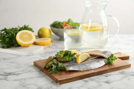 Salted herring fillets served with pickles, parsley and lemon on white marble tableの写真素材