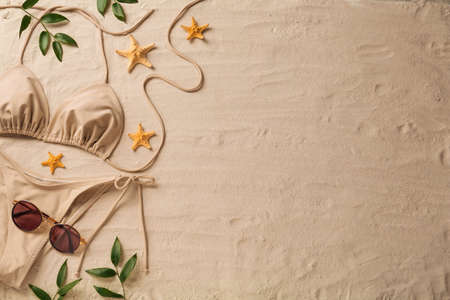 Stylish bikini, sunglasses, starfishes and leaves on sand, flat lay. Space for text