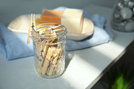 Many wooden clothespins in glass jar on white table, space for text