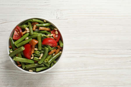 Delicious salad with green beans, mushrooms, pine nuts and tomatoes on white wooden table, top view. Space for textの写真素材